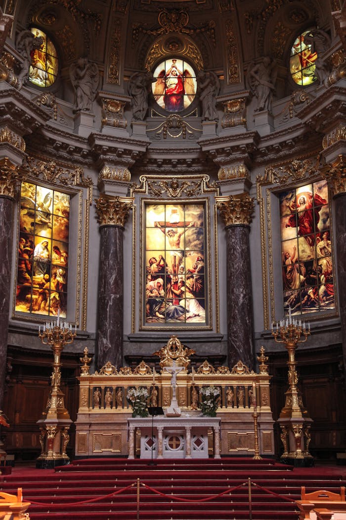 An elaborate church altar adorned with gold and intricate stained glass artwork depicting religious scenes.