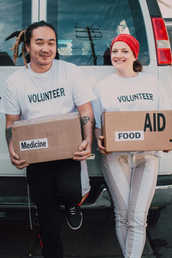 Two volunteers holding aid boxes with medicine and food labels, supporting charity causes.